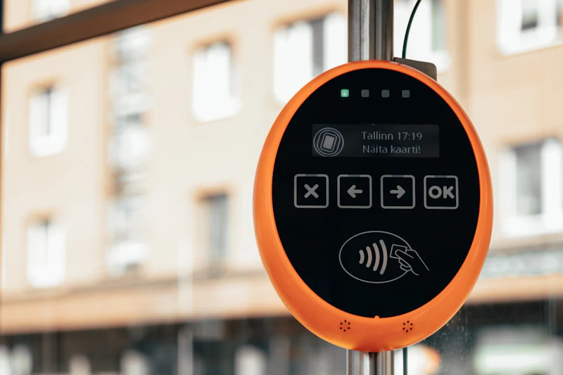 An orange contactless card validator mounted on a pole at a tram stop.